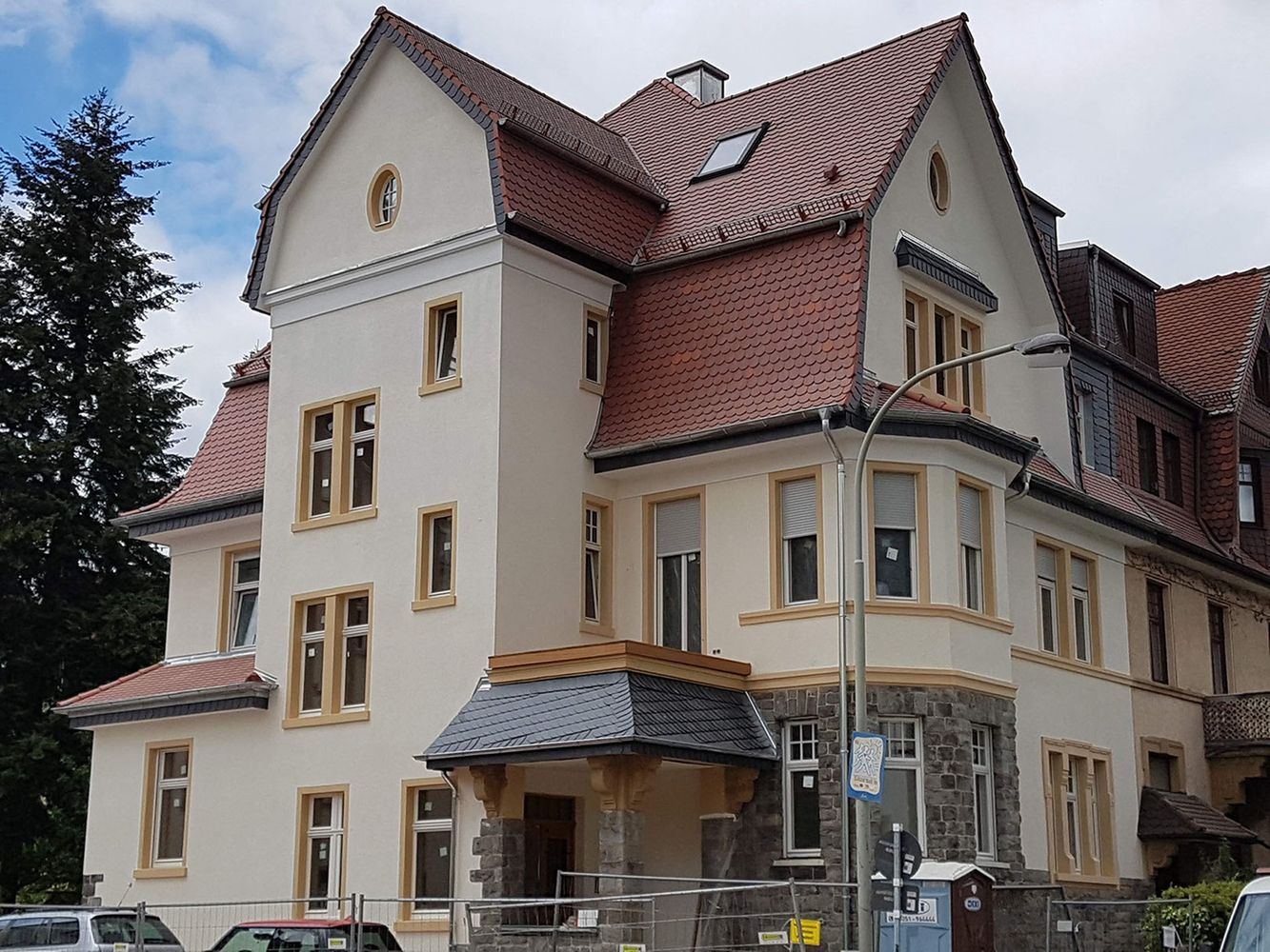 Haus mit rotem Ziegeldach, Dachgauben und Schornstein unter blauem Himmel